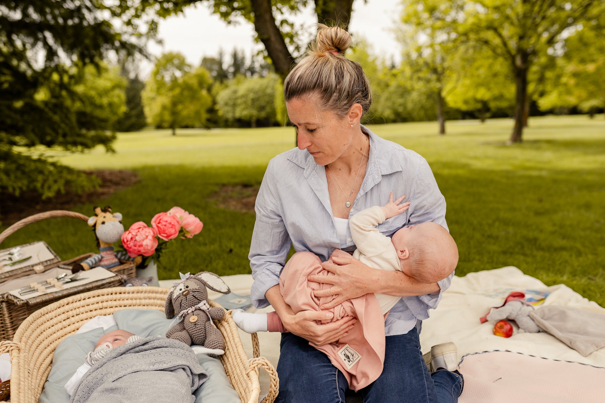 Woman holding a baby in a park with a picnic setup